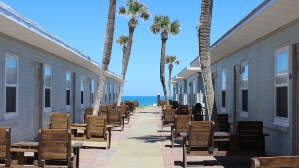 Un hotel frente a la playa con filas de sillas y mesas de madera alineadas a lo largo de un paseo central que conduce al océano.