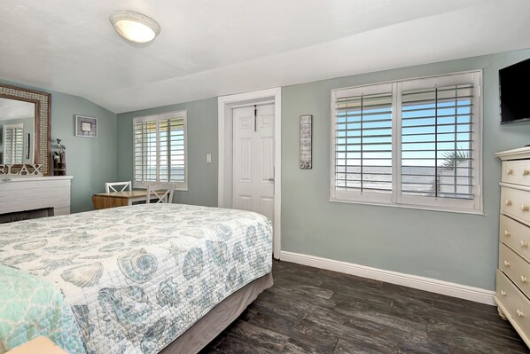A bedroom with a bed, a dresser, a chair, and a window with a view of the ocean.