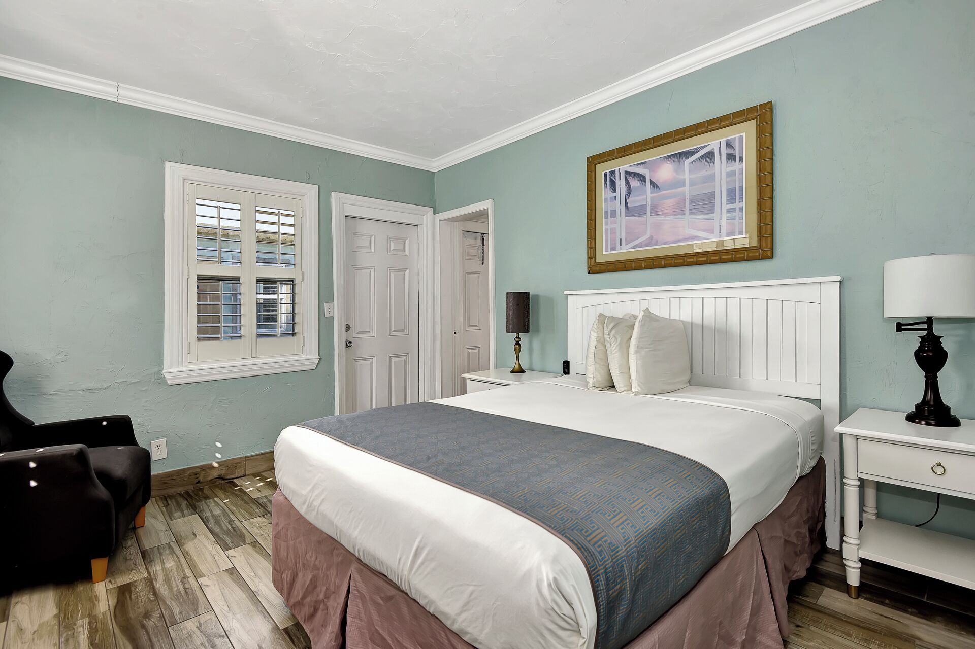 A bedroom with a bed, nightstands, a lamp, a chair, and a window with blinds.