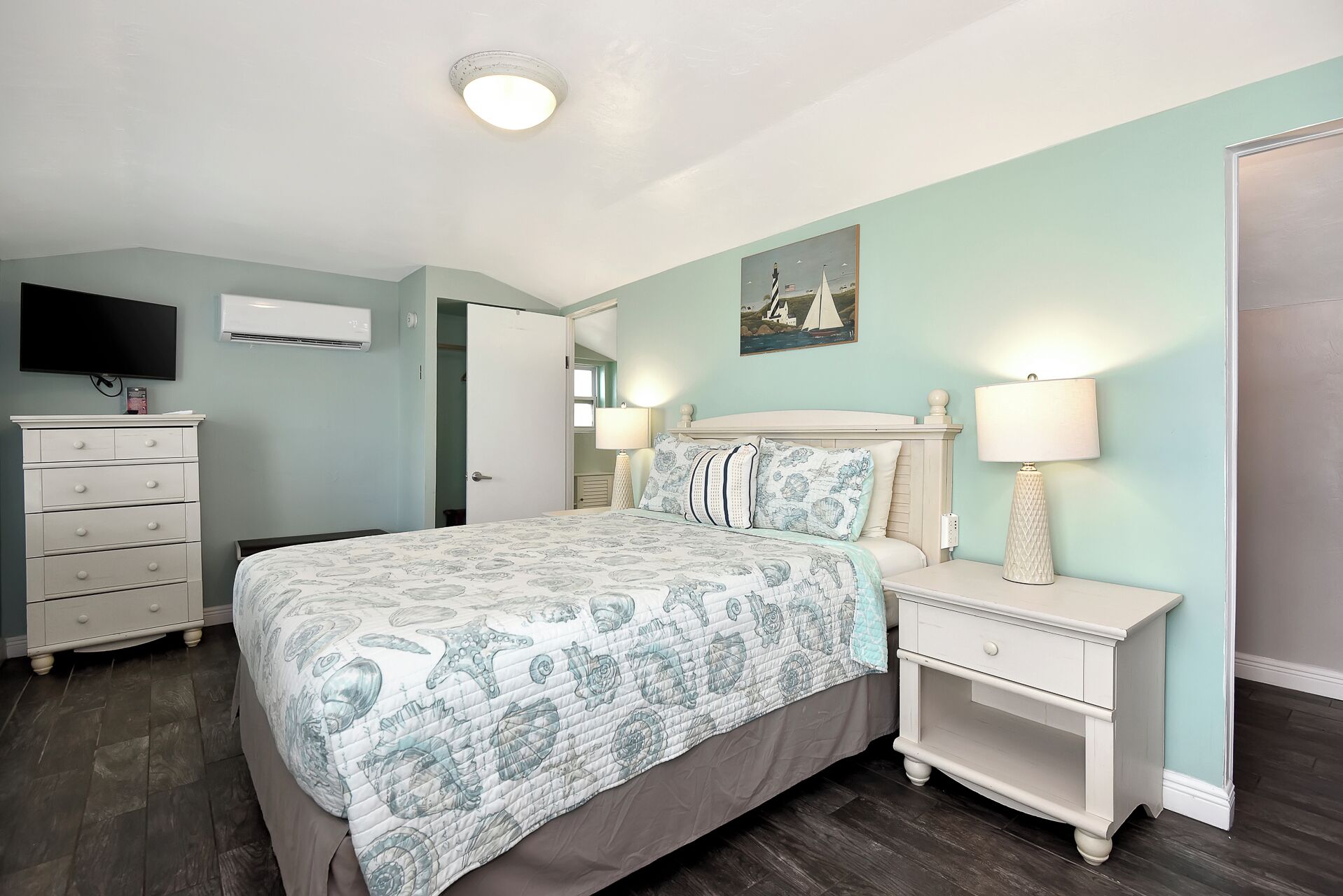 Une chambre à coucher comprenant un lit, des tables de chevet, une commode, un téléviseur et un tableau accroché au mur.