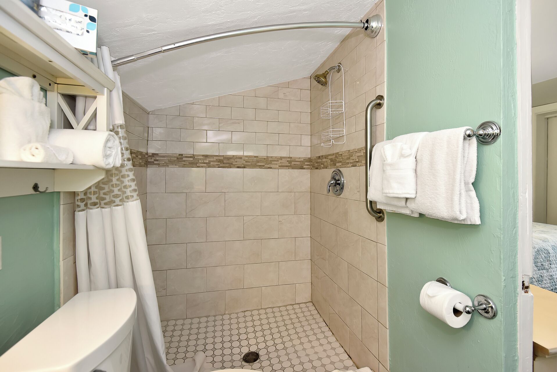 Dusche mit gebogener Glastür, Toilette und Handtuchhalter mit Handtüchern.