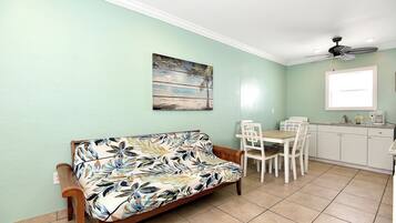 Un salon avec un canapé, une table à manger avec des chaises, un coin cuisine avec des placards et un ventilateur de plafond.