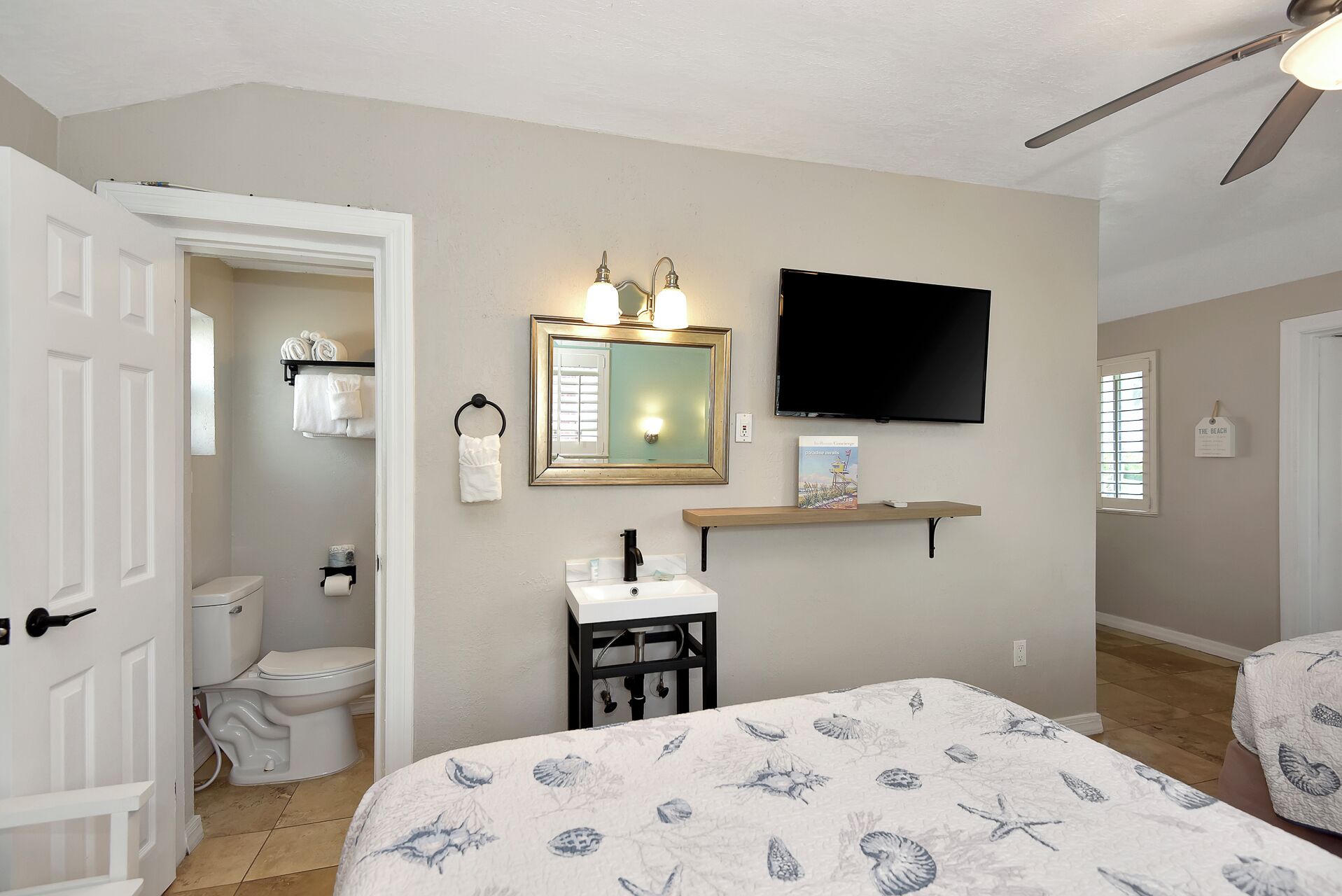 A bedroom with a bed, a TV, a bathroom with a toilet and sink, and a ceiling fan.