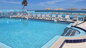 Una piscina con sillas de descanso y sombrillas, una palmera y vista al océano.