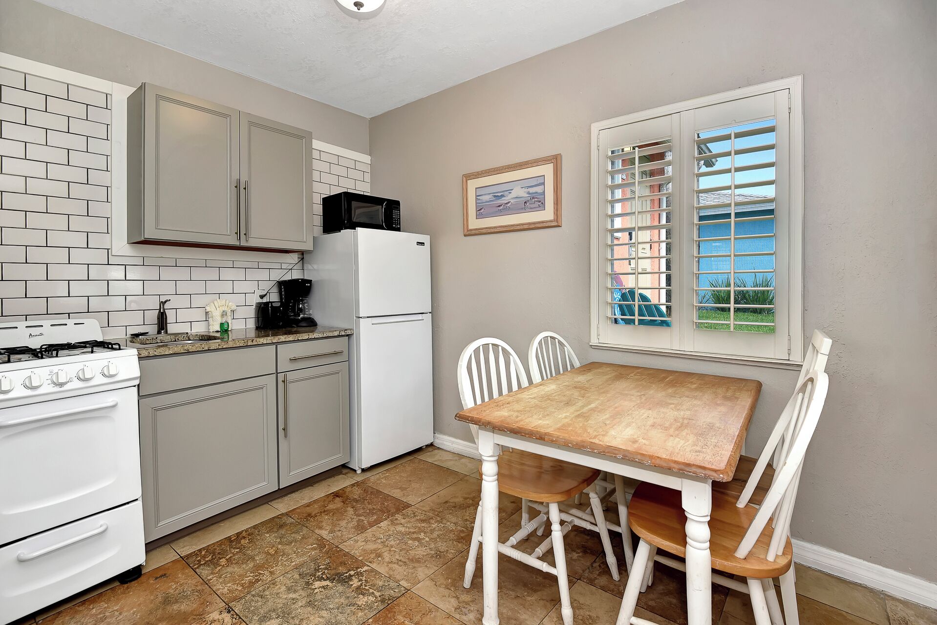 Une cuisine compacte avec des meubles blancs, une cuisinière, un réfrigérateur et une table à manger avec des chaises.