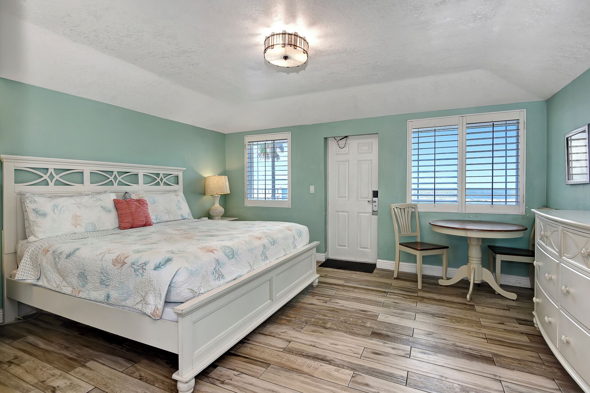 A bedroom with a bed, a chair, a table, and a dresser.