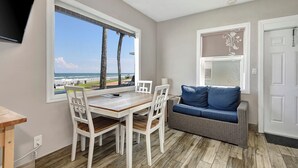 Una habitación con una mesa de comedor y sillas, un sofá azul y un ventanal con vistas a la playa y al océano.