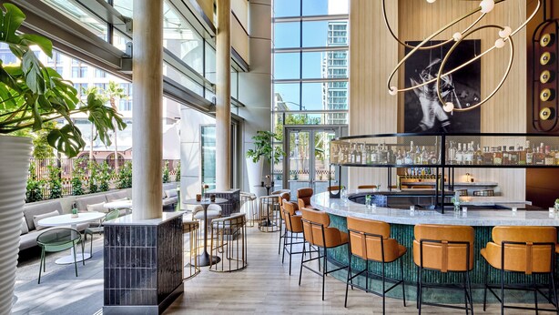 Un área de bar moderna con una barra curva, varios taburetes y un ventanal que ofrece vistas de la ciudad.