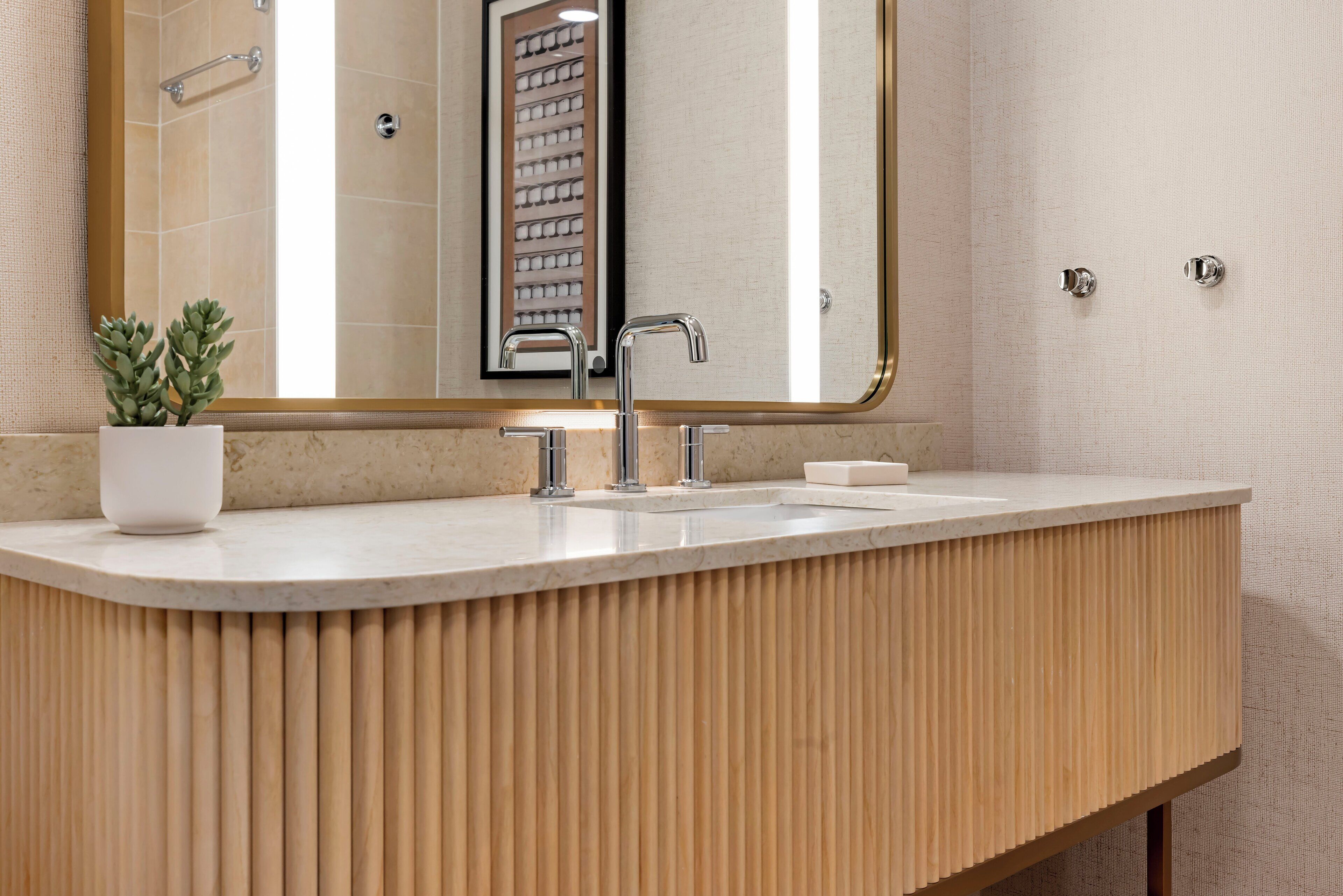 A modern bathroom with a curved vanity, a large mirror, and a potted plant.