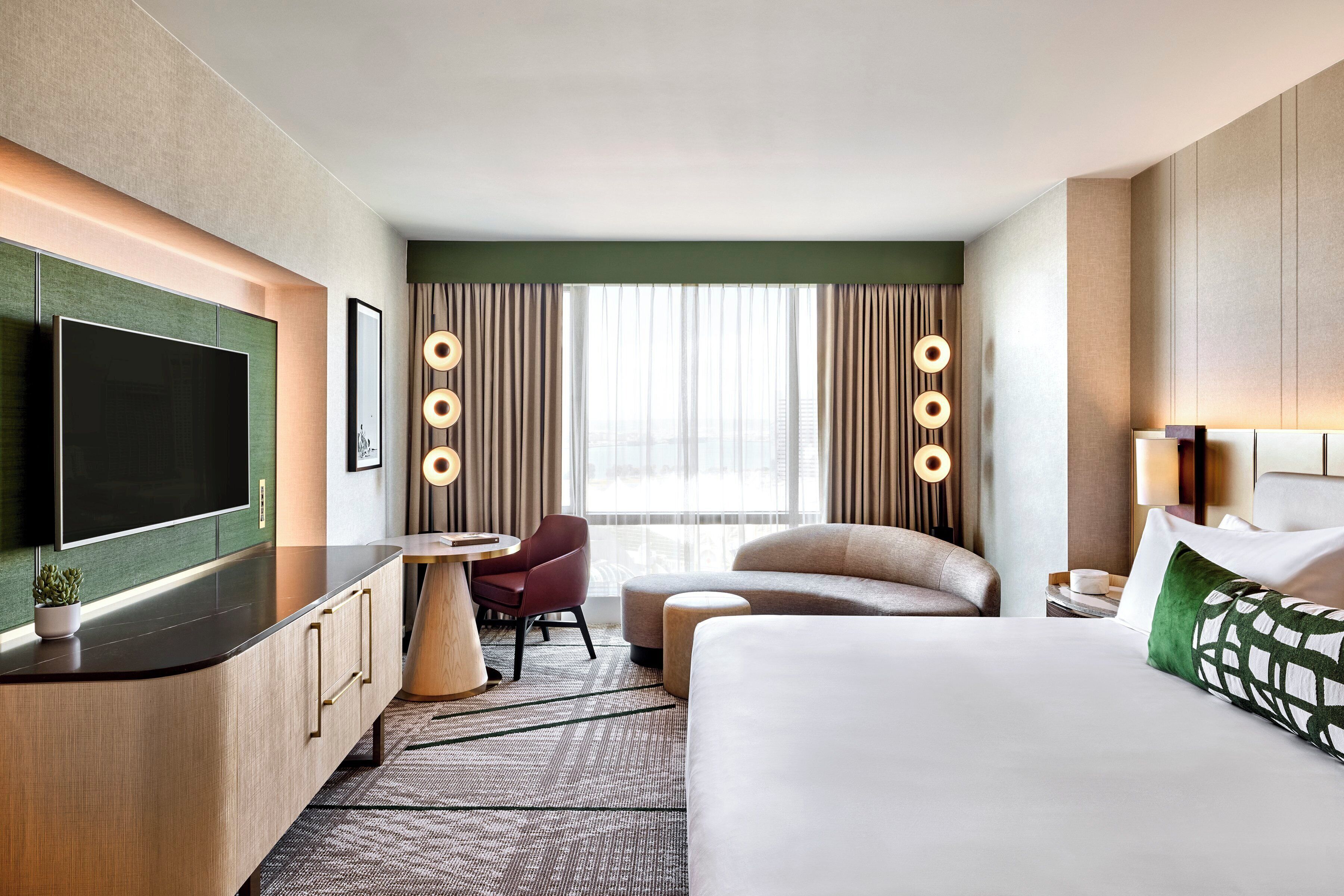 A hotel room with a large bed, a flat-screen TV, a desk, a chair, and a window with curtains.