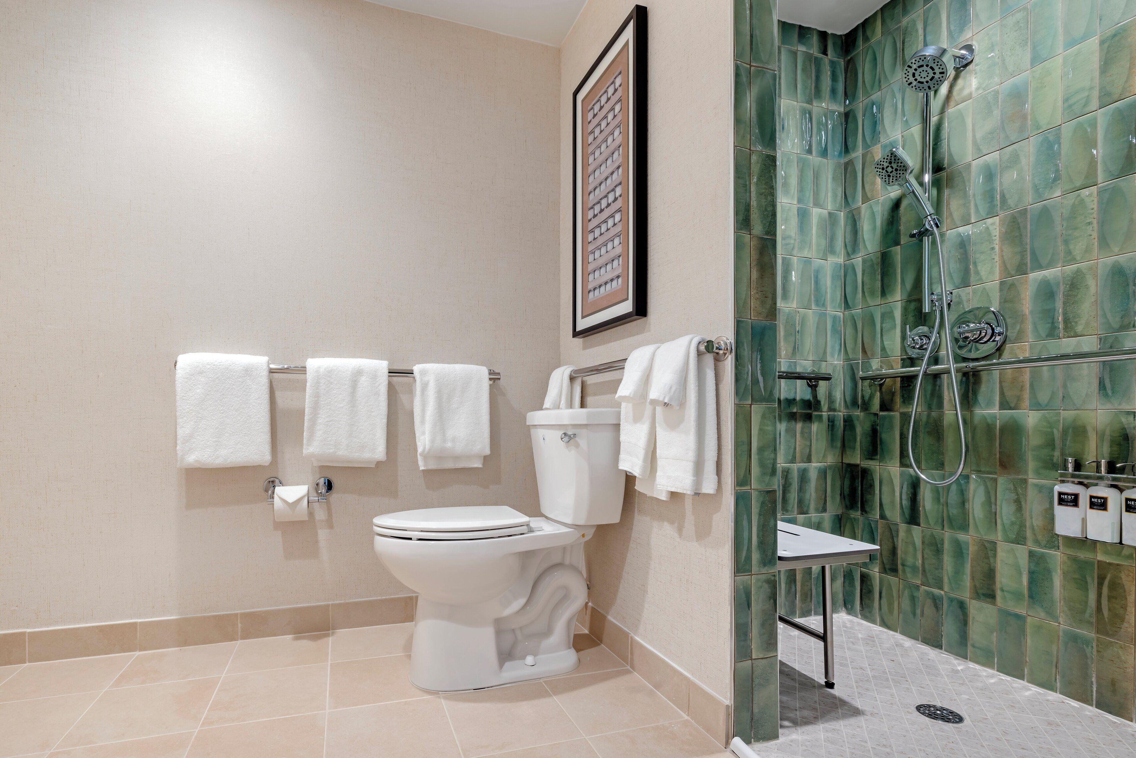Een badkamer met een toilet, meerdere witte handdoeken, een foto in een lijst aan de muur, en een douche met een groen betegelde wand.