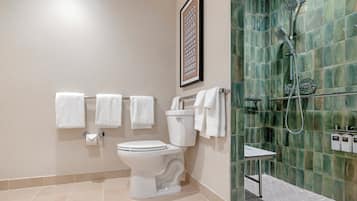 Een badkamer met een toilet, meerdere witte handdoeken, een foto in een lijst aan de muur, en een douche met een groen betegelde wand.