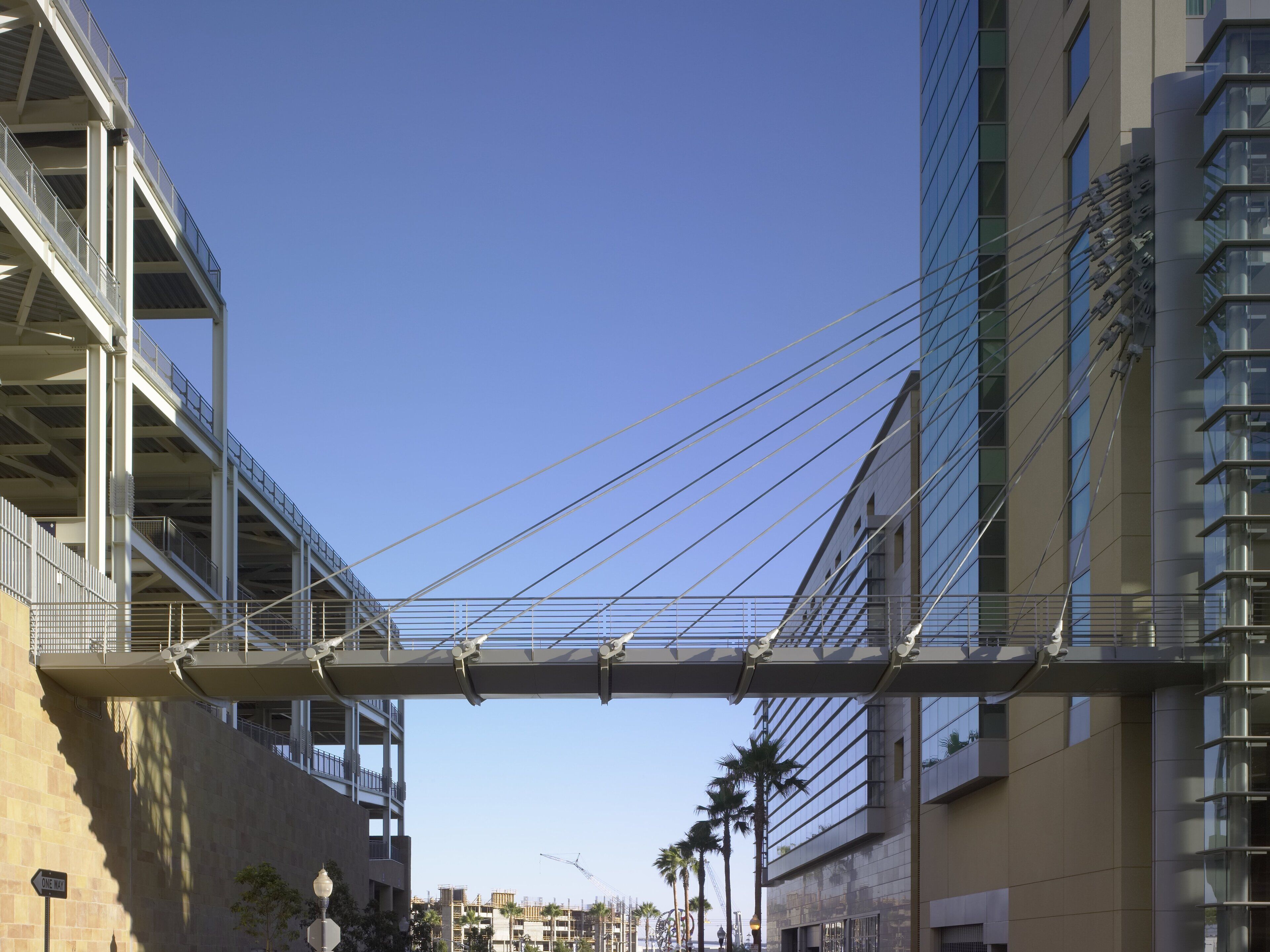 A pedestrian bridge with metal railings, connecting two buildings with modern architecture and glass facades.
