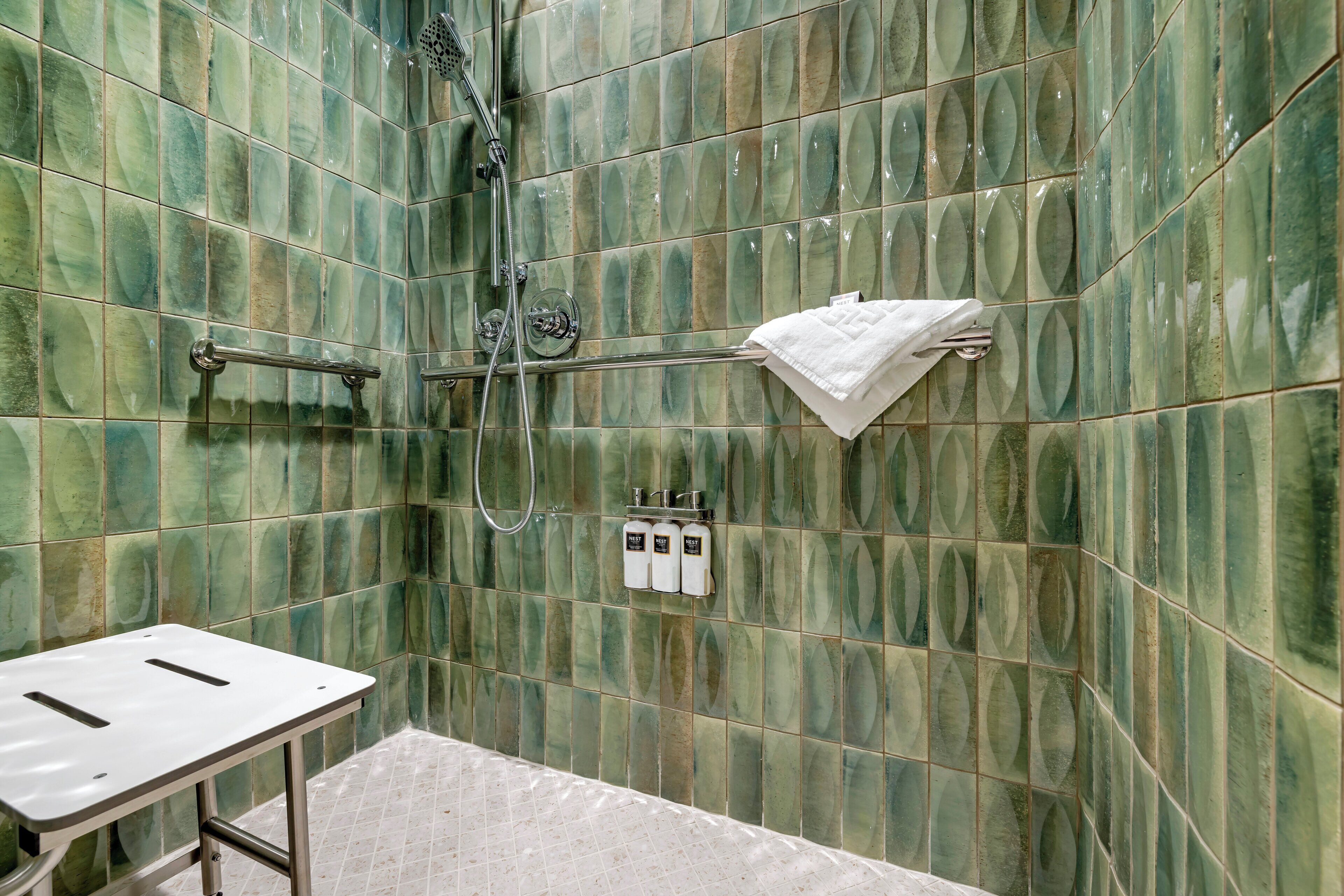 Une salle de bain avec des carreaux verts à motifs, une douche, un porte-serviettes et un lavabo.