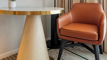 A modern room with a round table, a leather chair, a floor lamp, a framed picture, and a curtain.