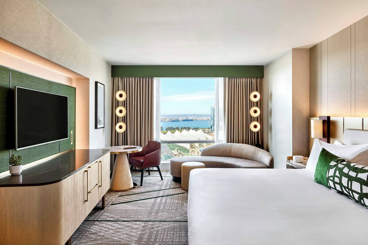 Habitación de hotel con una cama grande, televisión, escritorio y vista a la ciudad.