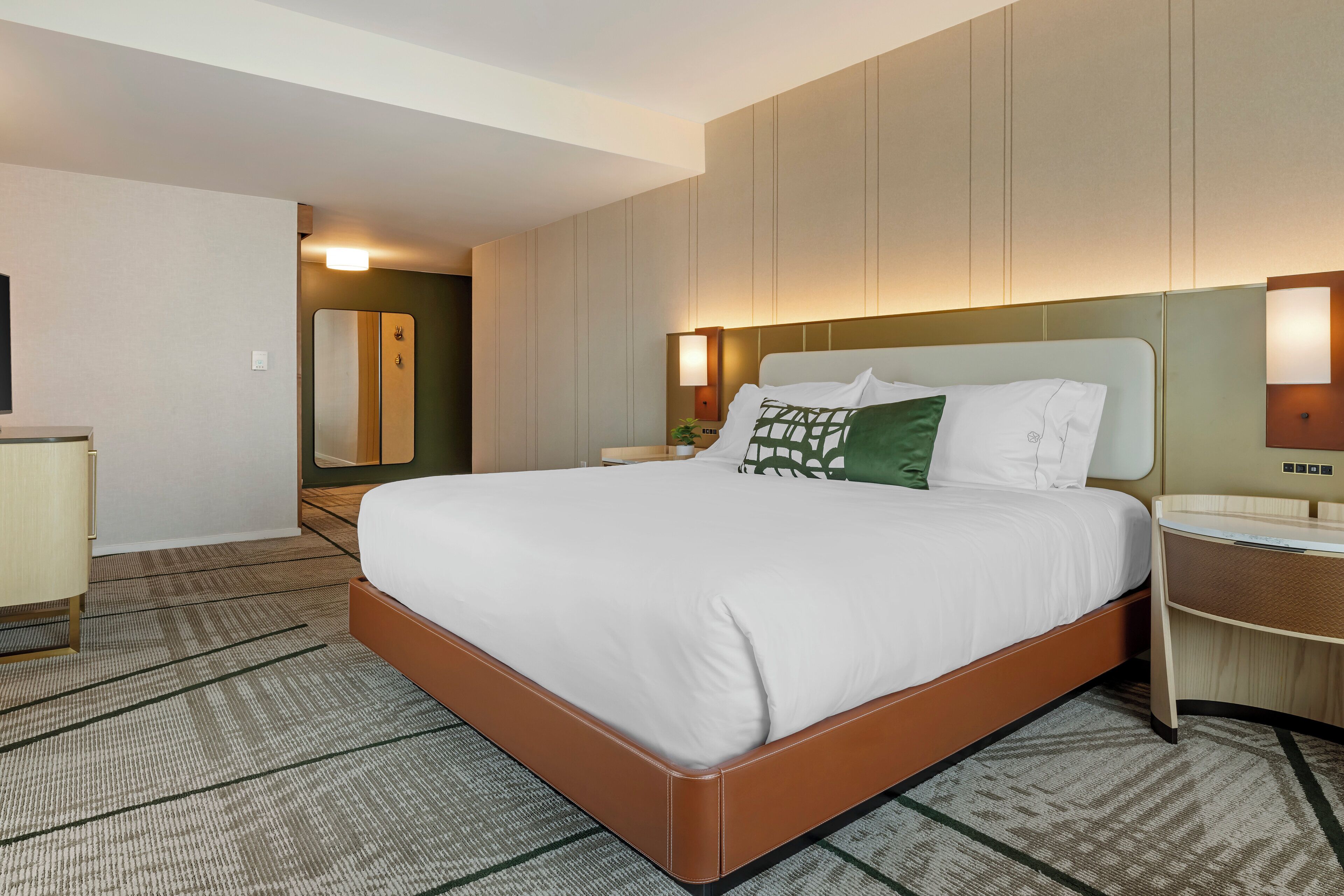 A hotel room with a large bed, bedside tables, a wardrobe, and a mirror.