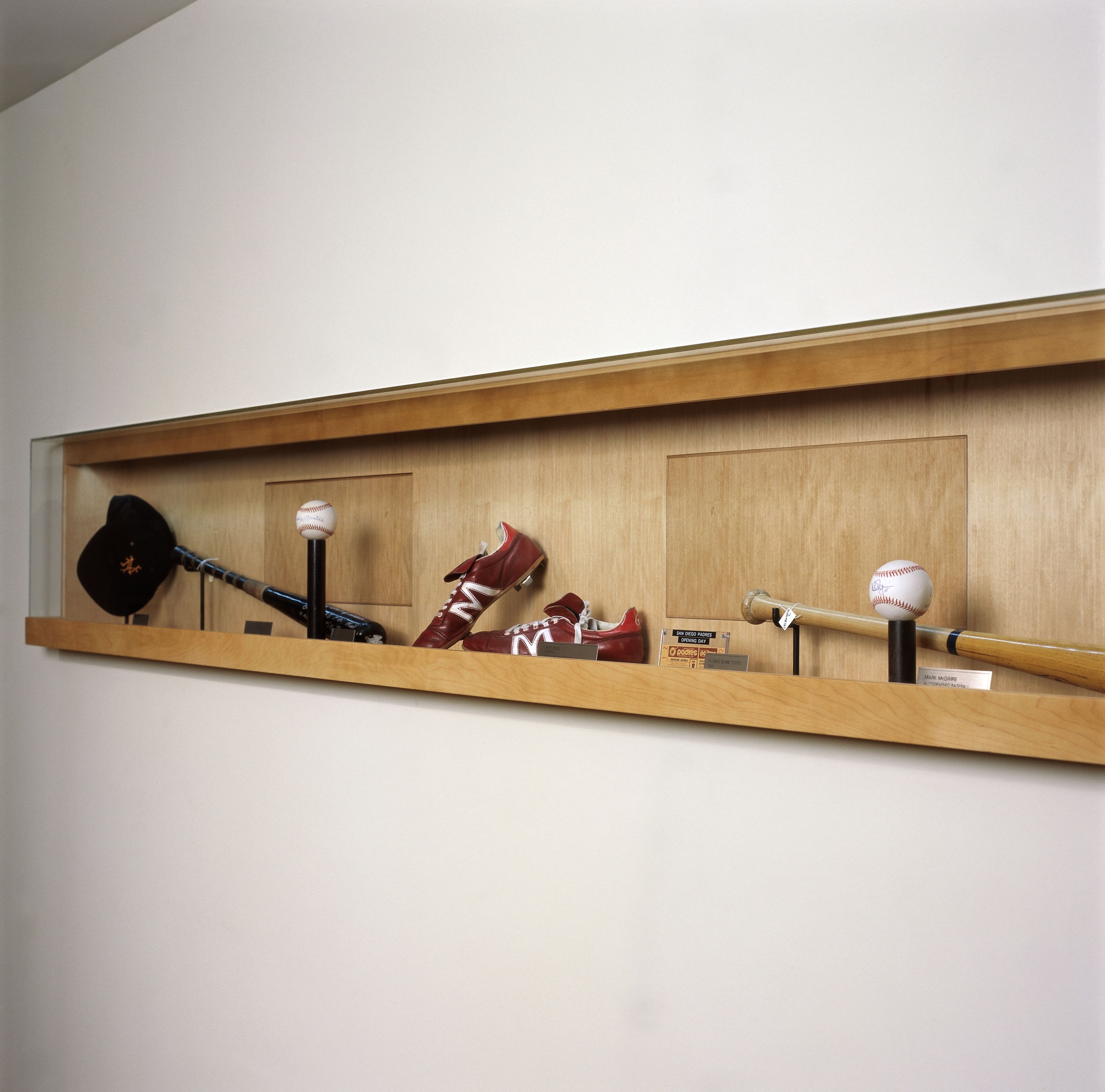 A wooden shelf with sports memorabilia including a baseball bat, a baseball, a pair of red shoes, and a baseball glove.