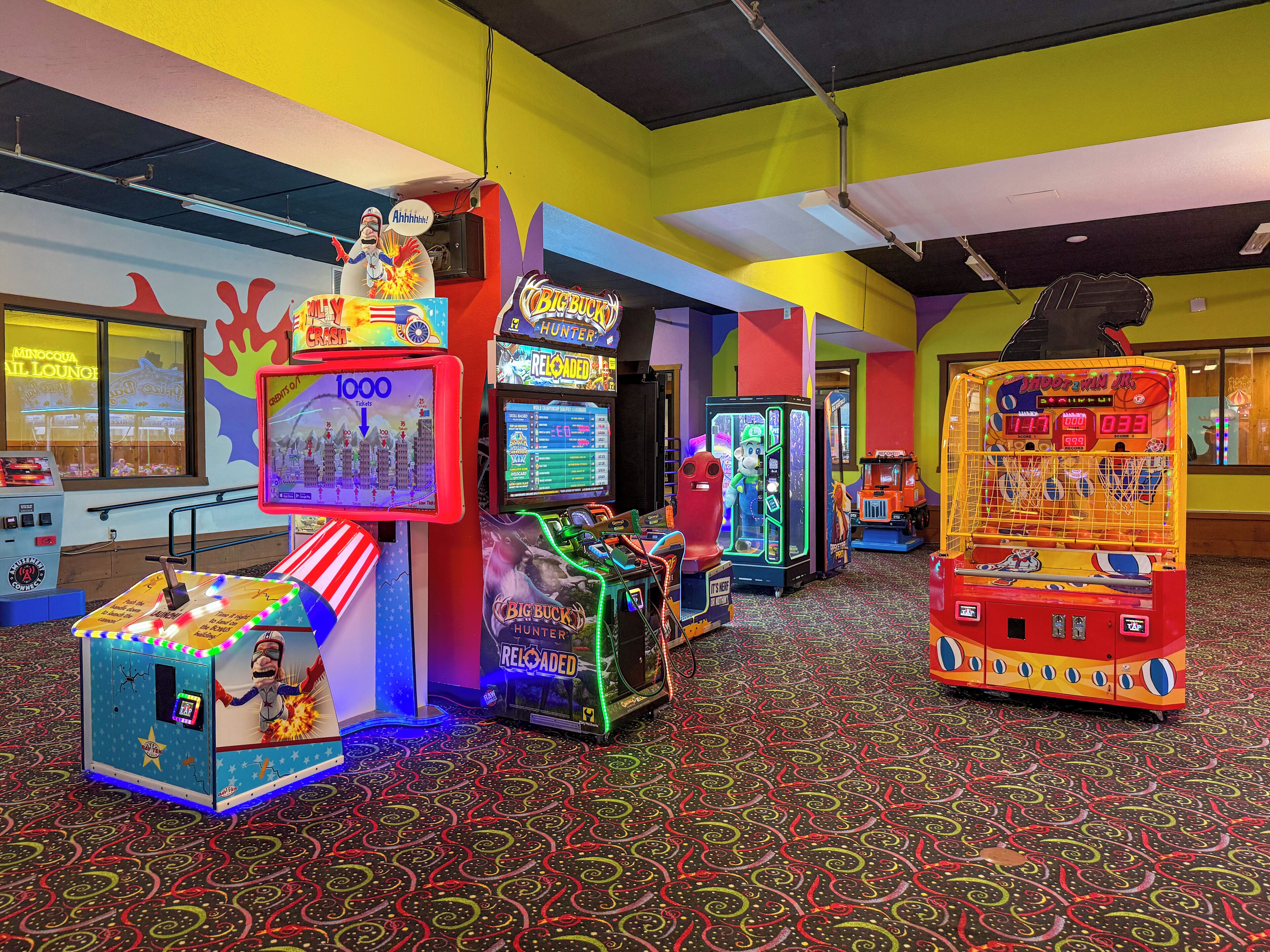 Una sala giochi luminosa con diverse macchine da gioco, tra cui una macchina con la grinfia e un gioco di tiro a canestro.