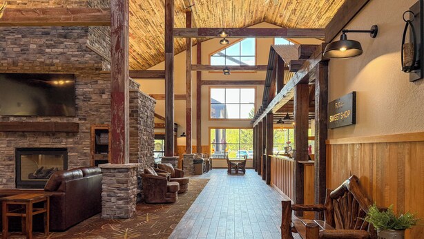 A spacious lodge interior with a stone fireplace, leather seating, a long wooden corridor, and a view of the outdoors. - The Waters Of Minocqua (Minocqua)