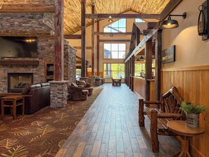 A spacious lodge interior with a stone fireplace, leather seating, a long wooden corridor, and a view of the outdoors. - The Waters Of Minocqua (Minocqua)