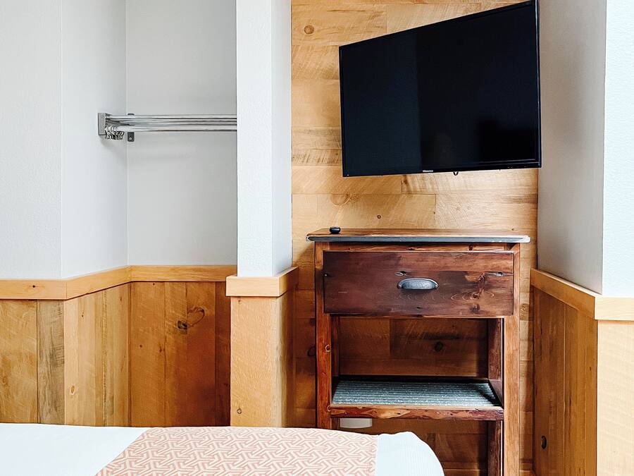 Een hotelkamer met een houten nagelak en een grote spiegel, en een bed met een beddengoed met een patroon.