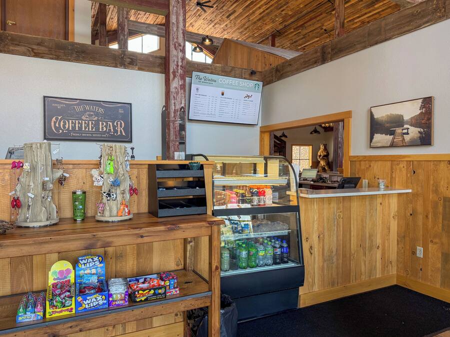 Interno di un bar con pareti in legno, una lavagna con il menu, un bancone caffetteria e una vetrina con portachiavi e snack.