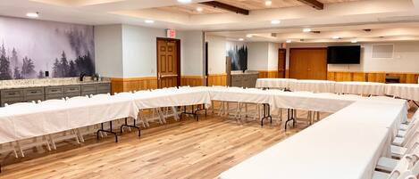 Une salle de conférence avec de longues tables et des chaises, un plancher en bois et une fresque murale.