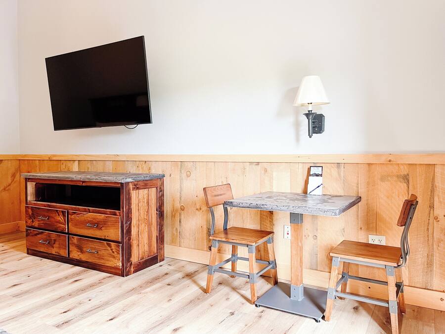 Una habitación con un armario de madera, una mesa con sillas, un televisor de pantalla plana y una lámpara de pared.