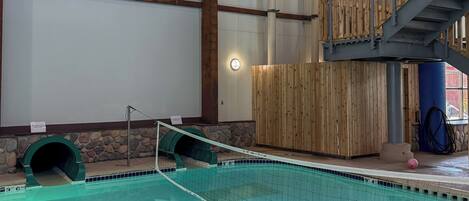 En indendørs swimmingpool med træterrasse og stenvæg.