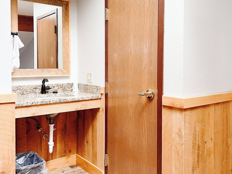 A bathroom with a wooden vanity, a sink, a mirror, and a door.