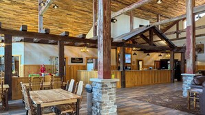 A rustic interior with wooden beams, a stone pillar, a wooden reception desk, and a dining area with wooden tables and chairs. - The Waters Of Minocqua (Minocqua)