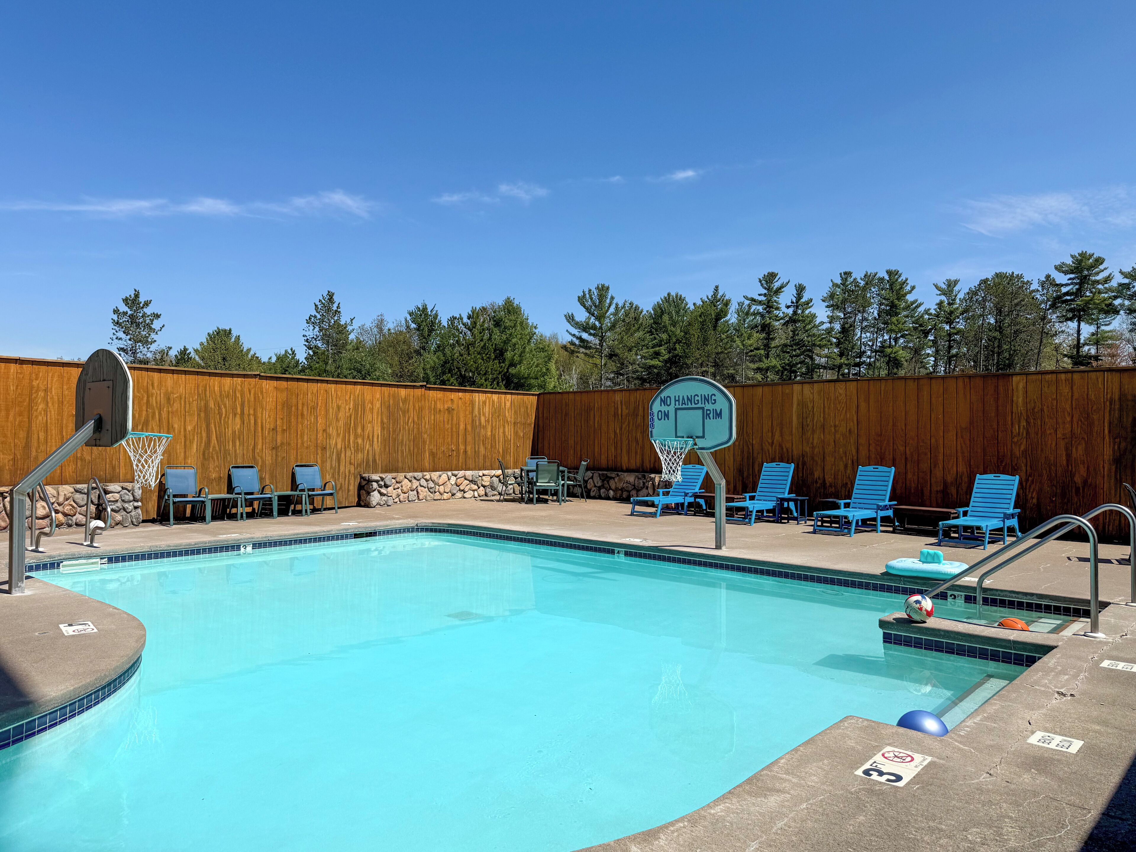 A swimming pool with a no-hanging-on rim sign, surrounded by blue lounge chairs and a wooden fence.
