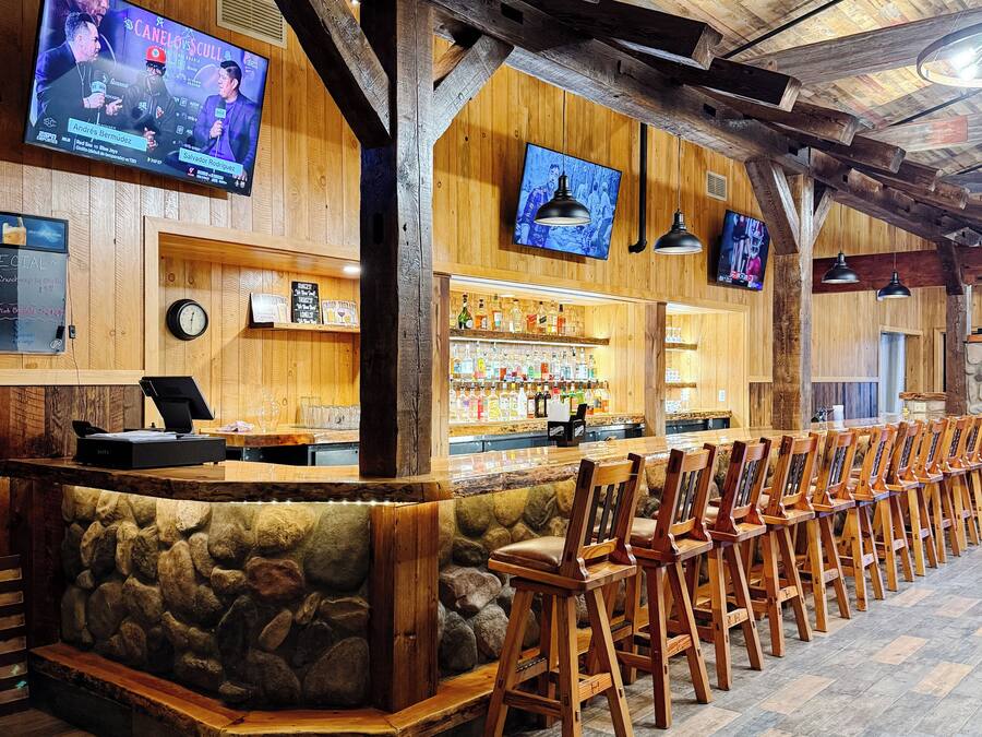 Zona de bar com paredes de madeira, detalhes em pedra e várias televisões.