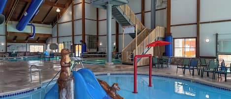 Una piscina interior con tobogán, escaleras de madera y zonas de estar.
