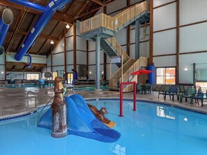 An indoor swimming pool with a slide, wooden stairs, and seating areas. - The Waters Of Minocqua (Minocqua)