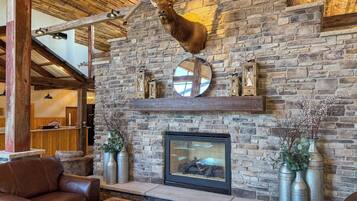 A rustic interior with a stone wall, a mounted deer head, a fireplace, leather seating, and metal vases.