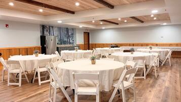 A conference room with round tables and white chairs, wooden floors, and a forest mural on the wall.
