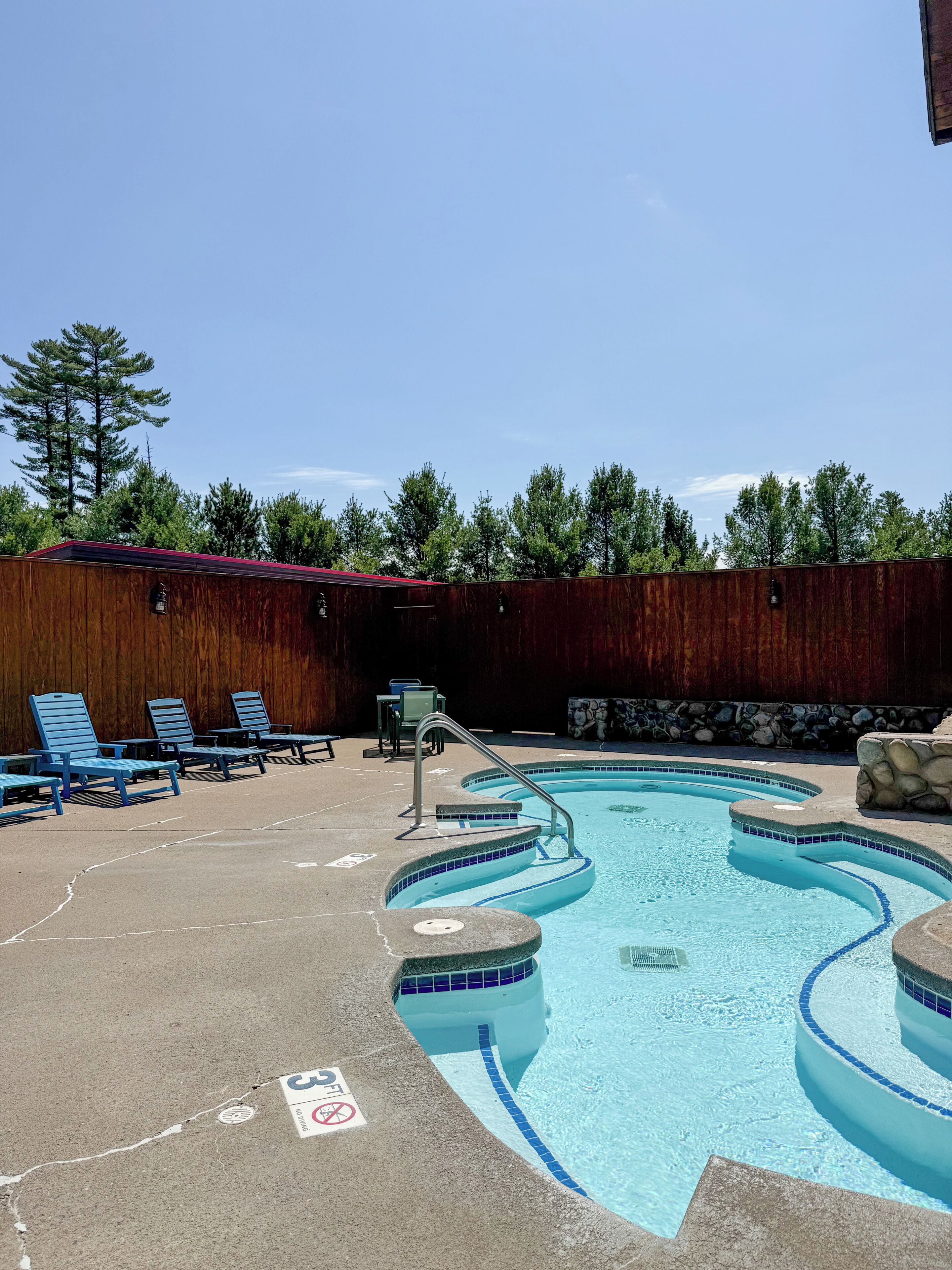 A swimming pool with blue-tiled edges, lounge chairs, and a wooden fence.