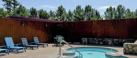 A swimming pool with blue-tiled edges, lounge chairs, and a wooden fence.