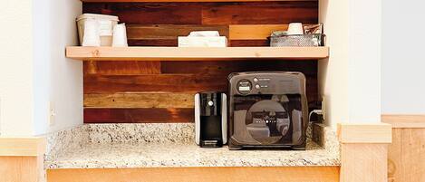 Une cuisine compacte avec un plan de travail en bois, un appareil à café et un appareil noir, probablement un four à micro-ondes ou un grille-pain, placés sous le plan de travail.