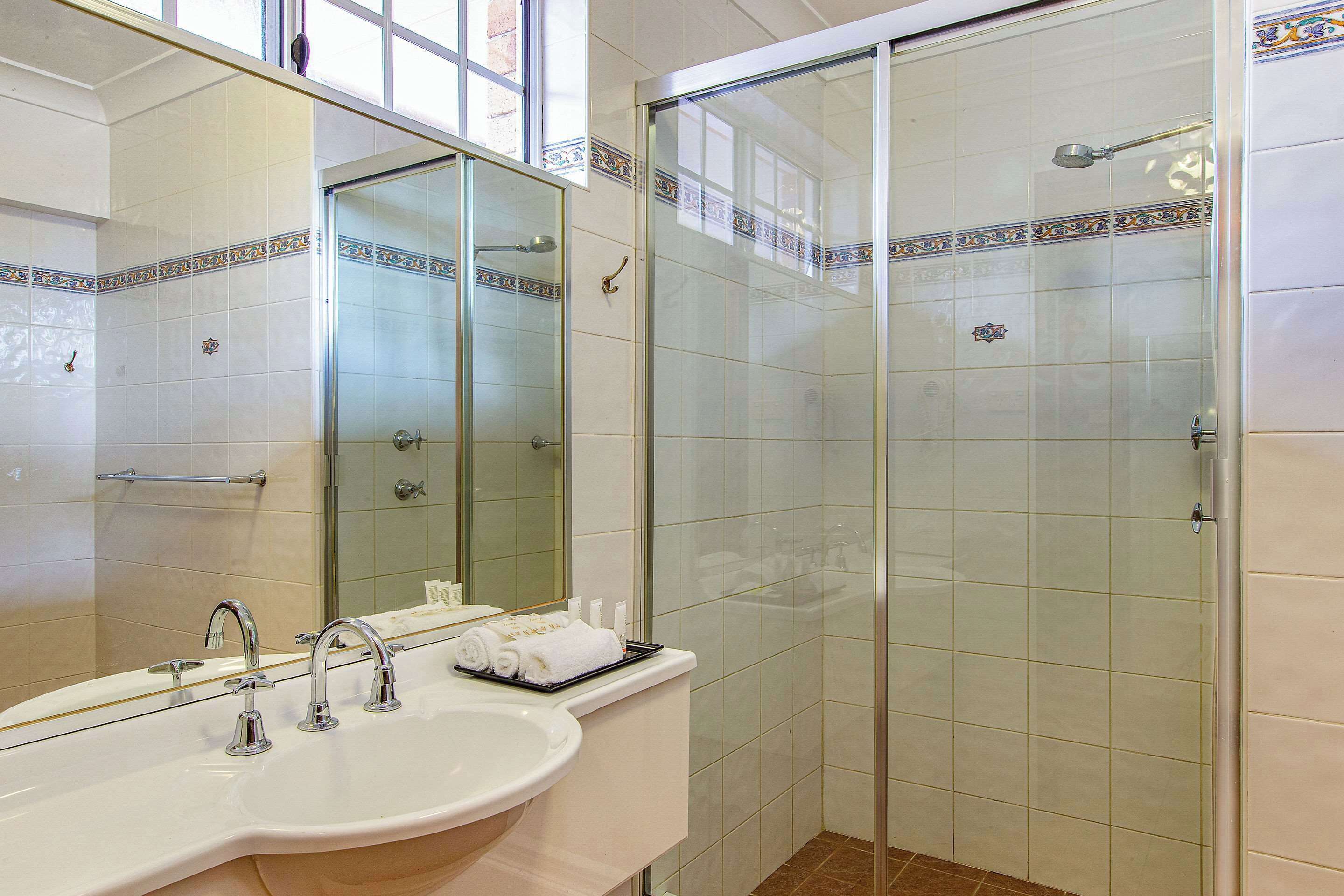 Une salle de bain avec une douche à parois de verre, un lavabo doté de deux robinets et un miroir au-dessus du lavabo.