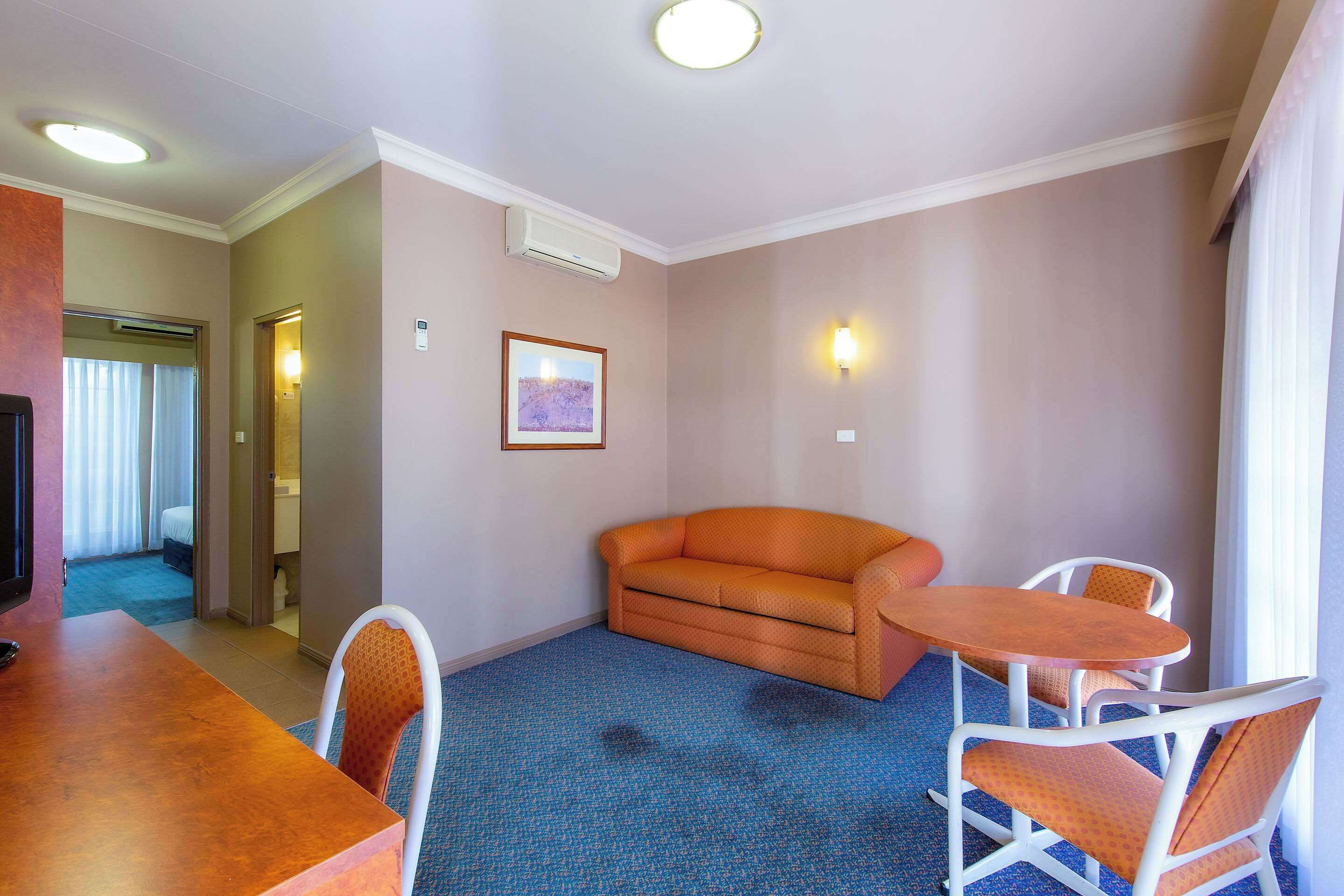 A hotel room with a blue carpet, an orange sofa, a wooden table, and white chairs.