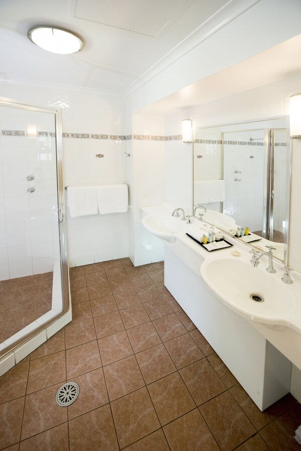 A bathroom with a glass-enclosed shower, two sinks, a large mirror, and a towel rack.