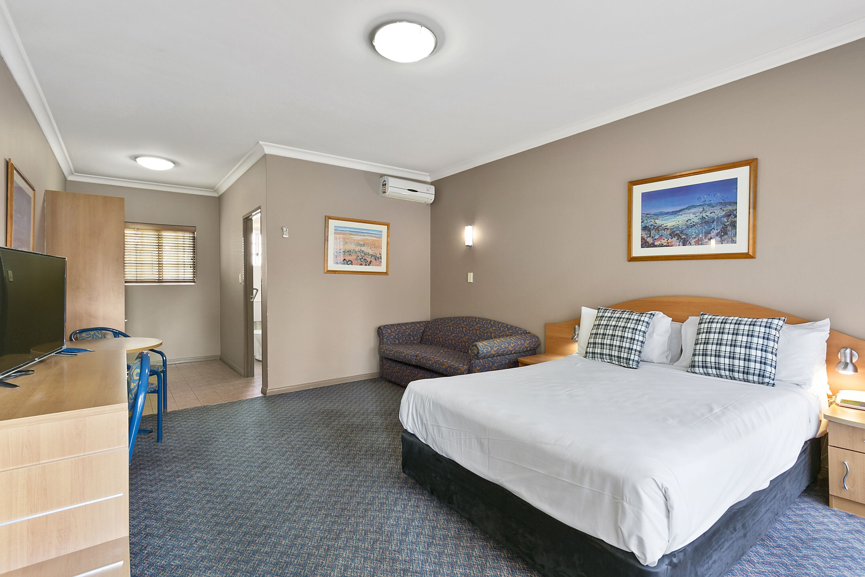 A hotel room with a bed, a desk, a chair, a sofa, and a TV.