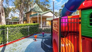 A playground with colorful play structures, a building with a green roof, and a sign that says "Welcome".