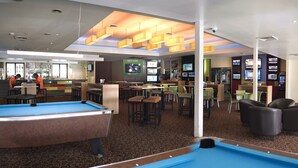 A pool table in a hotel lobby with a bar area and seating.