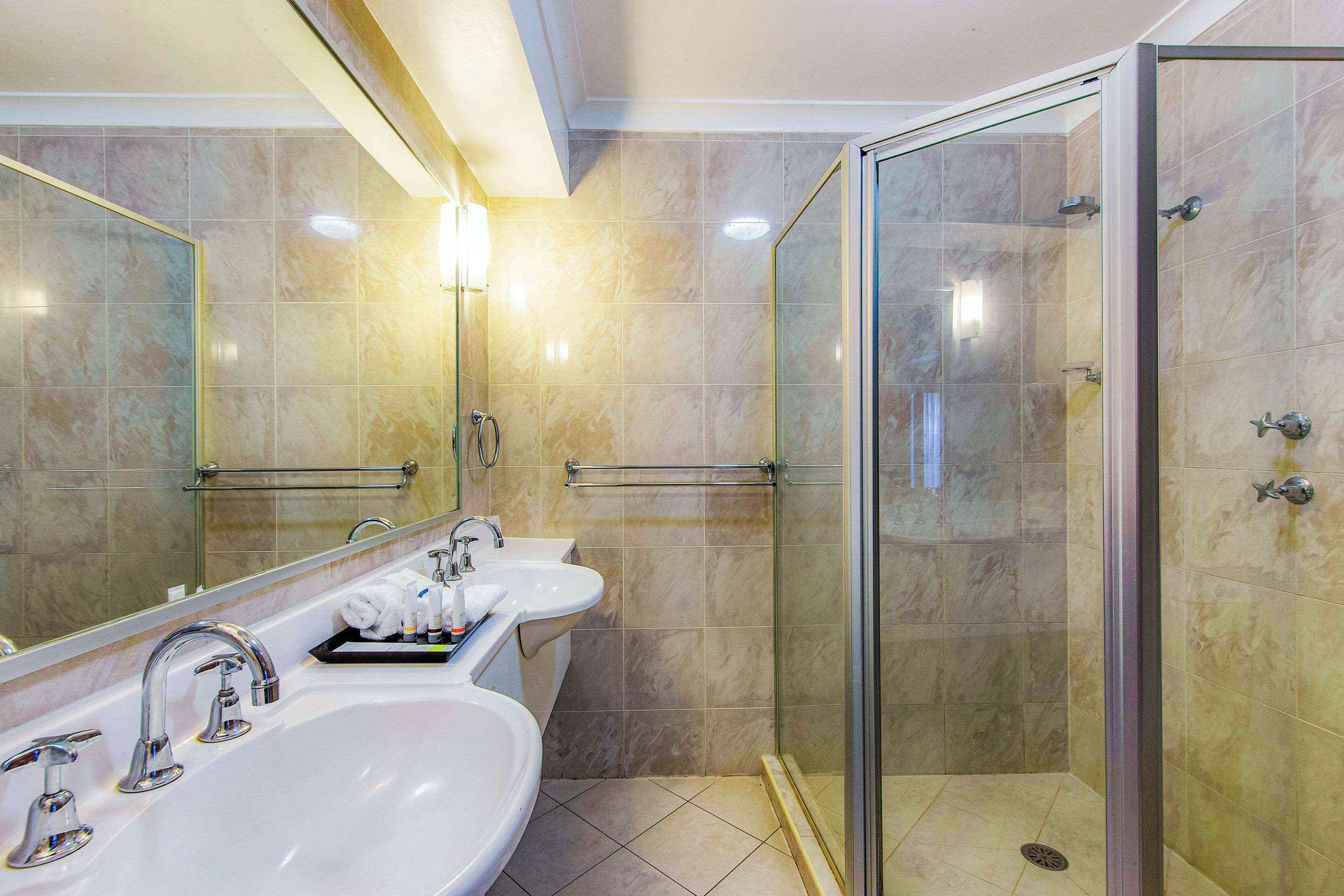 Un baño moderno con dos lavamanos, cabina de ducha de vidrio y un espejo grande.