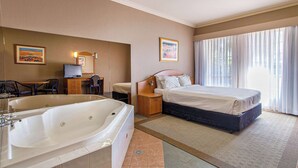 A hotel room with a large bathtub, a bed, a desk with a chair, and a television.