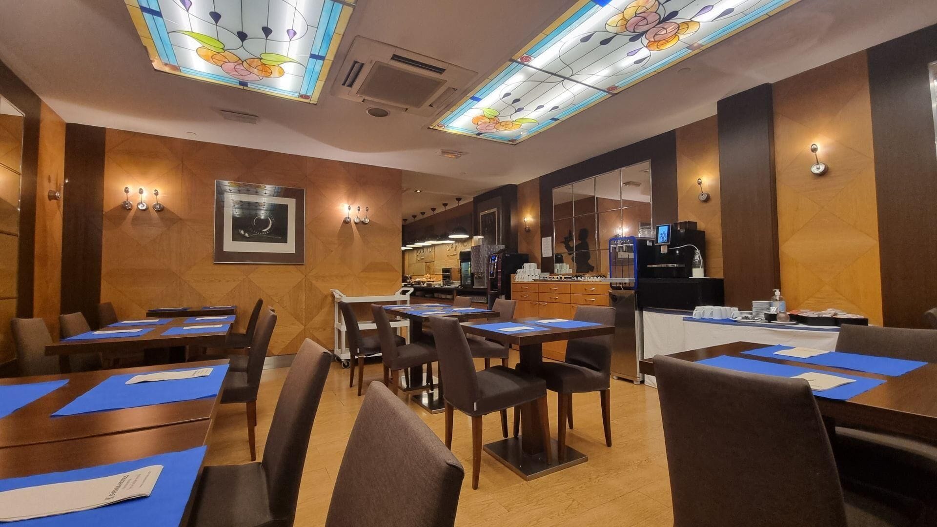 Een restaurantgedeelte in een hotel, met tafels, stoelen en een keuken op de achtergrond.